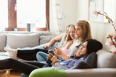 Side view of teenage girls watching TV while relaxing on sofa at home - MASF02875