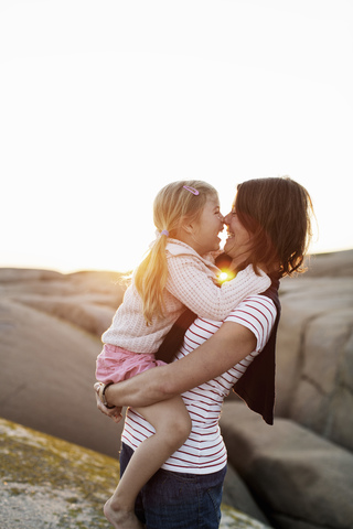 Seitenansicht der Mutter, die ihre Tochter gegen den klaren Himmel bei Sonnenuntergang trägt, lizenzfreies Stockfoto