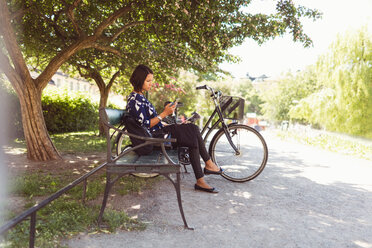 Seitenansicht einer Geschäftsfrau, die auf einer Parkbank sitzend ein Smartphone benutzt - MASF02879