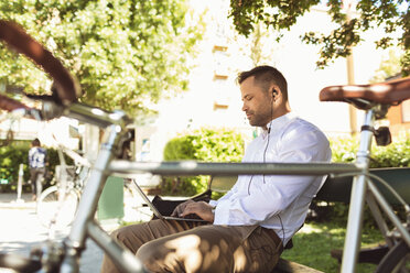 Side view of businessman using laptop while sitting on park bench - MASF02880