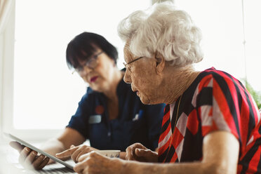 Senior woman using digital tablet with caretaker at home - MASF02893