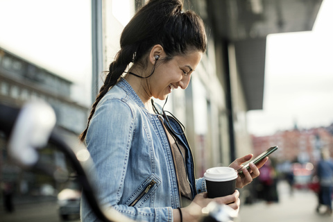 Seitenansicht einer Frau mit Smartphone und Kaffeetasse in der Stadt, lizenzfreies Stockfoto