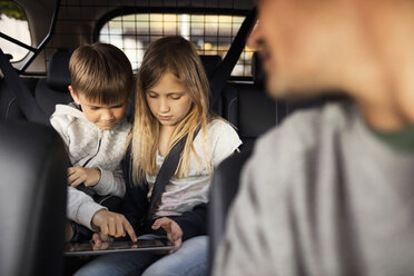 Geschwisterkind benutzt digitales Tablet, während es im Auto sitzt, mit Vater im Vordergrund - MASF02903