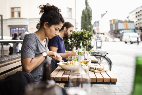 Seitenansicht eines Mannes und einer Frau beim Mittagessen in einem Straßencafé in der Stadt, lizenzfreies Stockfoto