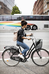 Seitenansicht einer Frau, die ein Mobiltelefon benutzt, während sie mit dem Fahrrad auf einer städtischen Straße fährt - MASF02908