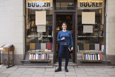 Porträt einer glücklichen Frau, die ein Buch hält, während sie vor einer Buchhandlung steht - MASF02910