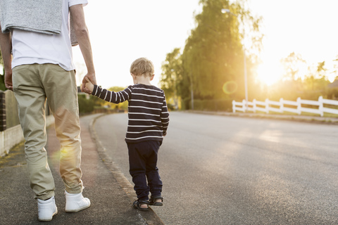 Rückansicht eines Jungen, der mit seinem Vater auf der Straße spazieren geht und dabei die Hände hält, lizenzfreies Stockfoto