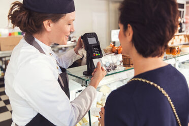 Saleswoman assisting female customer with credit card reader at grocery store - MASF02924