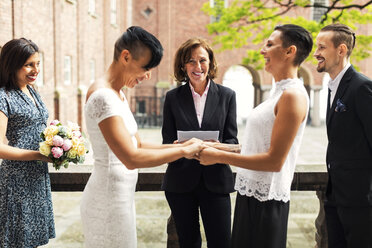 Priester und Gäste betrachten ein fröhliches lesbisches Paar, das sich an den Händen hält - MASF02929