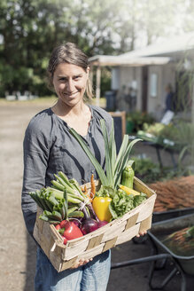 Porträt einer glücklichen Frau, die Gemüse in einem Korb trägt - MASF02933
