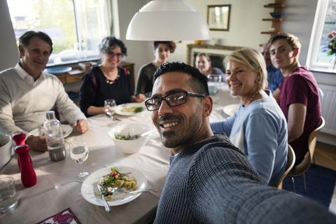 Porträt eines lächelnden Mannes, der ein Selfie mit Familie und Freunden bei einer Dinnerparty macht, lizenzfreies Stockfoto