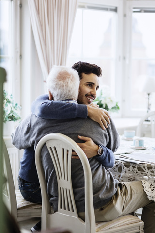 Junge Pflegerin umarmt älteren Mann im Pflegeheim, lizenzfreies Stockfoto