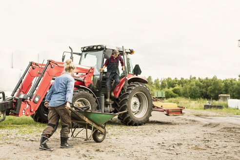 Frau schiebt Schubkarre in Richtung Mann und Traktor auf dem Bauernhof - MASF02953