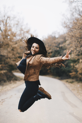 Porträt einer glücklichen jungen Frau, die im Freien in die Luft springt, lizenzfreies Stockfoto