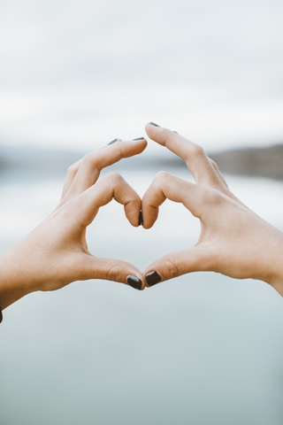 Woman's hands forming heart-shape in front of lake, close-up stock photo