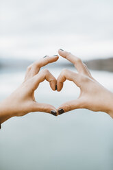 Woman's hands forming heart-shape in front of lake, close-up - OCAF00204