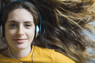 Portrait of smiling young woman with headphones lying on bed - KKAF00977