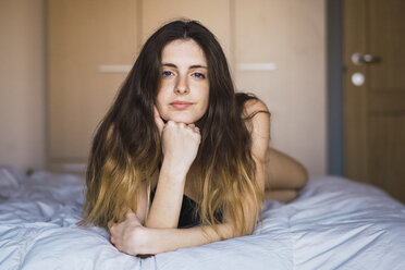 Porträt einer jungen Frau mit Haaren auf dem Bett liegend - KKAF00990