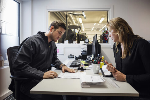 Owner and customer discussing over documents in auto repair shop - MASF02967