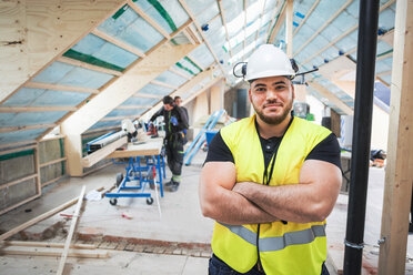 Porträt eines selbstbewussten Arbeiters, der mit verschränkten Armen auf einer Baustelle steht - MASF02973