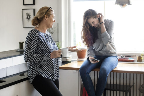 Mother talking with happy daughter using smart phone in kitchen - MASF02977