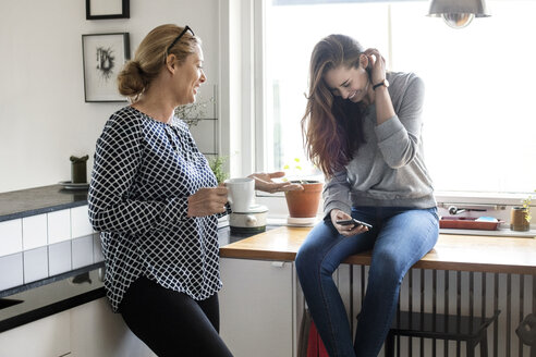 Mutter spricht mit glücklicher Tochter, die ein Smartphone in der Küche benutzt - MASF02977