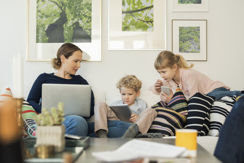 Mother and kids using technologies on sofa at home stock photo