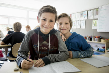 Porträt eines glücklichen Jungen mit Büchern auf dem Schreibtisch im Klassenzimmer - MASF02987