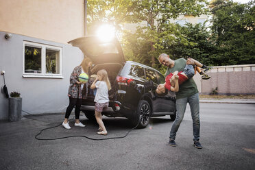 Verspielter Vater und Sohn mit Frau und Mädchen, die in einem Hinterhof neben einem Auto stehen - MASF03004