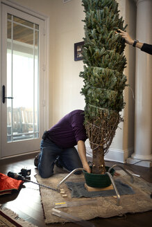 Man decorating Christmas tree at home - CAVF36262