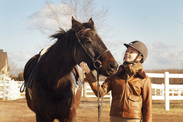 Teenager-Mädchen, das ein Pferd streichelt, während es auf einem Feld steht - CAVF36274