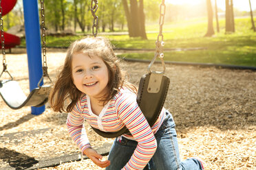 Porträt eines glücklichen Mädchens, das auf einem Spielplatz schaukelt - CAVF36278