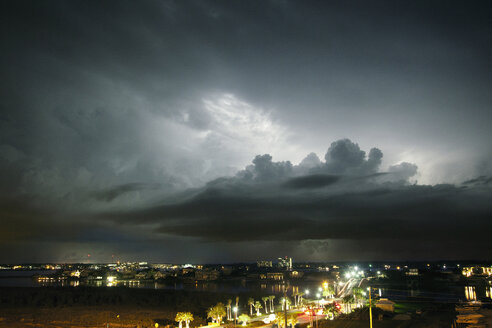 Storm clouds over illuminated city street at night - CAVF36297