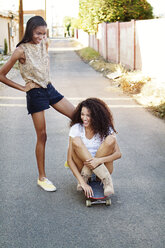 Glückliche Freunde mit Skateboard auf der Straße in der Stadt - CAVF36337