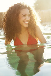 Happy woman looking away while swimming in pool on sunny day - CAVF36340