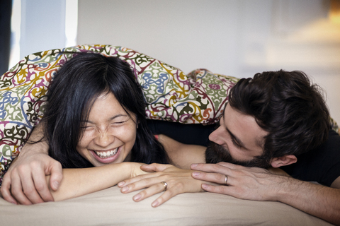 Glückliches Paar im Gespräch, während es zu Hause auf dem Bett liegt, lizenzfreies Stockfoto