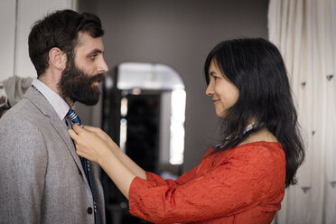 Smiling woman adjusting necktie on husband at home - CAVF36369