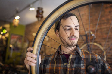 Mann betrachtet in einer Werkstatt stehend ein Fahrradrad - CAVF36415