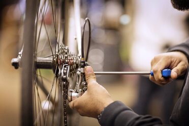 Ausgeschnittenes Bild eines Mannes, der ein Fahrrad in einer Werkstatt repariert - CAVF36418
