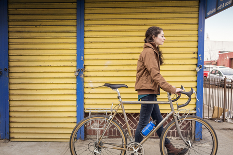 Seitenansicht einer Frau mit Fahrrad auf einem Fußweg in der Stadt, lizenzfreies Stockfoto