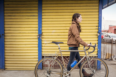 Seitenansicht einer Frau mit Fahrrad auf einem Fußweg in der Stadt - CAVF36430