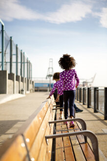 Rückansicht von Mädchen, die auf einer Holzbank an der Promenade gegen den Himmel laufen - CAVF36458