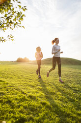 Mutter und Tochter laufen auf Gras im Park gegen den Himmel bei Sonnenuntergang - MASF03030