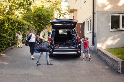Mann und Frau laden Gepäck in den Kofferraum, während der Junge das Elektroauto auflädt, lizenzfreies Stockfoto