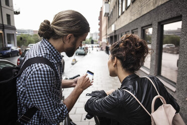 Mann zeigt einem Freund auf dem Bürgersteig in der Stadt sein Smartphone - MASF03039