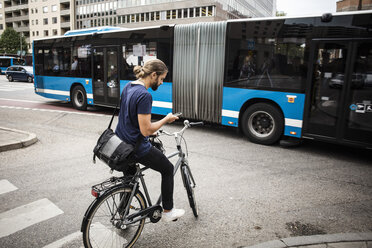 Man with bicycle using mobile phone while standing on city street against articulated bus - MASF03041