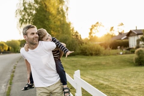 Happy father piggybacking son while standing by grassy field during sunset stock photo