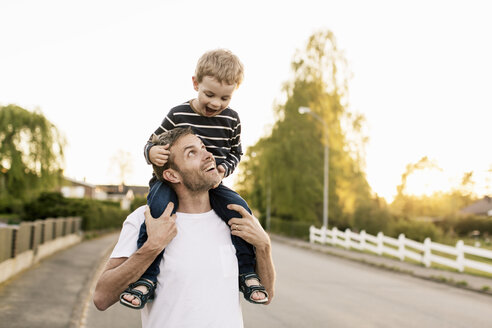 Glücklicher Vater, der seinen Sohn auf den Schultern trägt, während er auf der Straße gegen den klaren Himmel steht - MASF03050