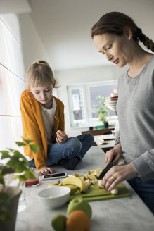 Mädchen sieht Mutter beim Schneiden von Obst auf der Küchentheke zu Hause an - MASF03052