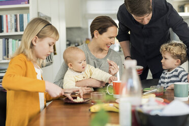 Happy family eating breakfast at table in living room - MASF03053